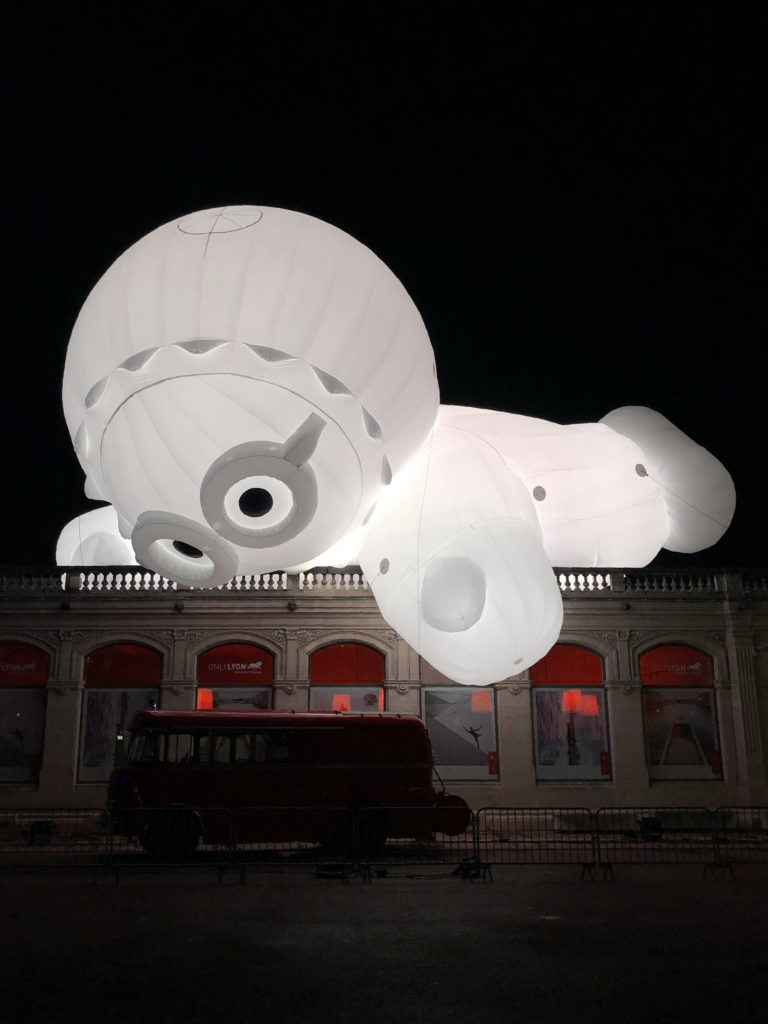 Un personnage gonflable, éclairé de l'intérieur, joue avec un camion place Bellecour, à Lyon.